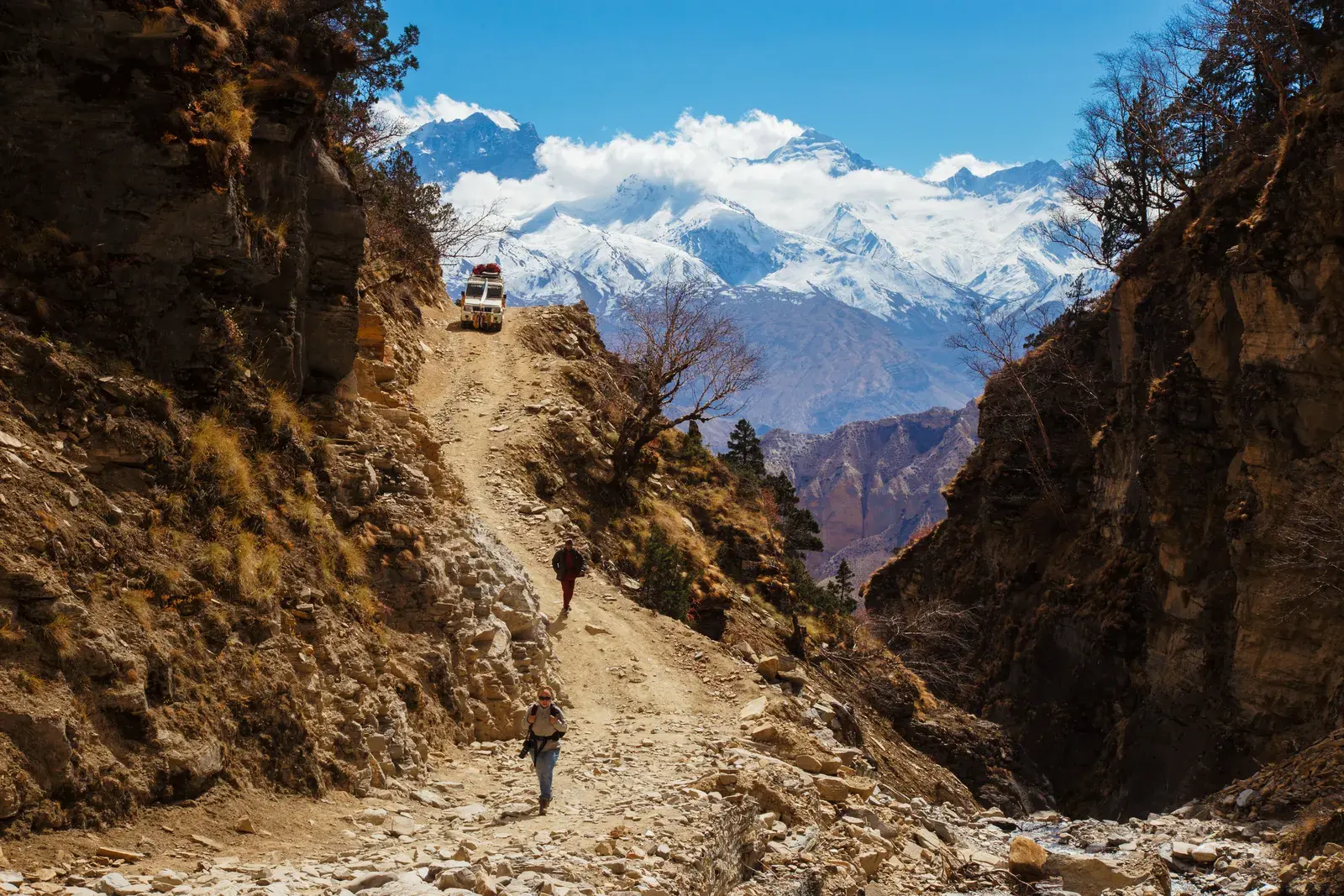 Jeep on a dirt trail below snow peaks, Upper Mustang